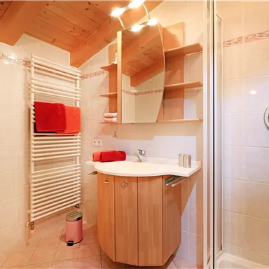 Ein modernes Badezimmer mit einem Holzschrank und einem großen Spiegel. Die Wände sind hell gefliest und es gibt Handtücher in leuchtendem Rot.