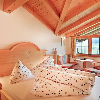 Ein gemütliches Schlafzimmer mit Holzdekor und großen Fenstern. Das Zimmer ist hell und freundlich, mit einem kleinen Tisch und Stühlen.