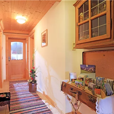 Ein einladender Flur mit Holzdecke und buntem Teppich. Eine Kommode mit Postkarten und einer Pflanze verleiht dem Raum ein gemütliches Ambiente.