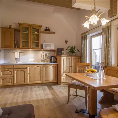 Eine gemütliche Küche mit Holzschränken und einem Essbereich. Große Fenster sorgen für viel Tageslicht.