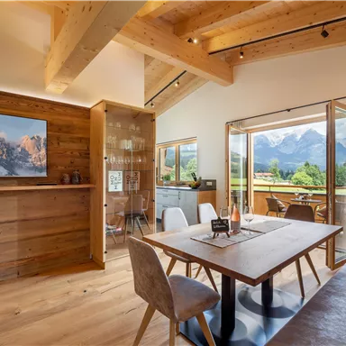 Ein modernes Wohnzimmer mit Holzdekor und großen Fenstern. Im Hintergrund sind Berge zu sehen, und der Raum ist hell und einladend.