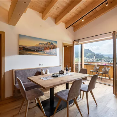 Ein heller Essbereich mit Holzdecke und einem großen Tisch. Durch die Fenster blickt man auf eine malerische Berglandschaft.