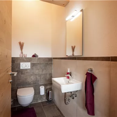 Ein modernes Badezimmer mit einer Toilette und einem kleinen Waschbecken. Die Wände sind hell und stilvoll gestaltet.