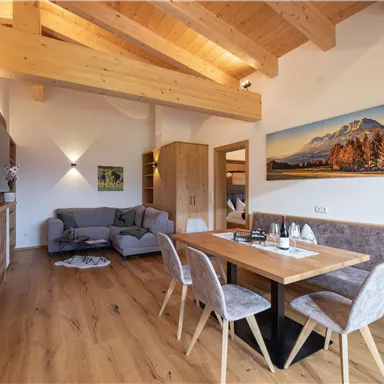 Ein modern eingerichteter Wohnbereich mit offener Holzdecke. Ein Esstisch und eine gemütliche Sitzecke bieten einen einladenden Raum zum Entspannen.