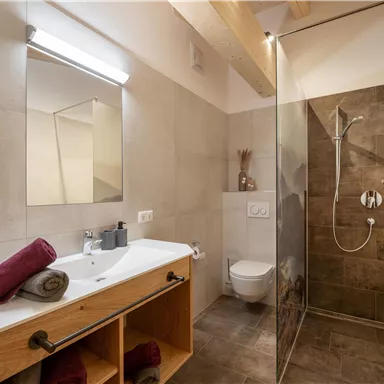 Ein modernes Badezimmer mit einer Dusche und einem Waschbecken. Die Einrichtung ist schlicht und elegant mit Holz- und Steinakzenten.