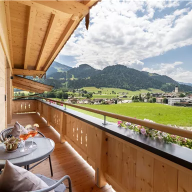 Ein Balkon mit einem Blick auf grüne Wiesen und Berge. Der Himmel ist klar und sonnig, ideal für Entspannung im Freien.