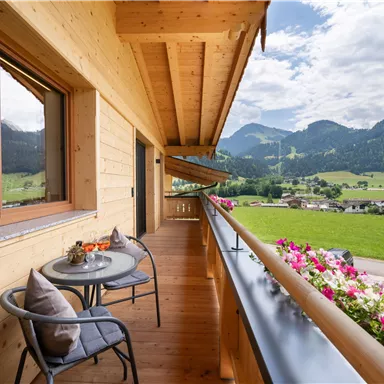 Ein schöner Balkon mit einem Blick auf die Berge und grünen Wiesen. Auf dem Tisch stehen frische Blumen und Früchte.