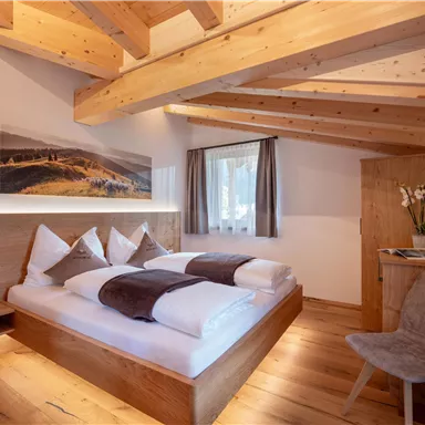 Ein gemütliches Schlafzimmer mit Holzmöbeln und einem Doppelbett. Die Wände sind hell und es gibt große Fenster mit Aussicht.