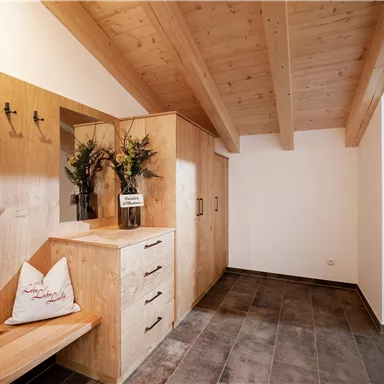 Ein helles und modernes Eingangsbereich mit Holzregalen und einer gemütlichen Bank. Frische Blumen in einer Vase verleihen dem Raum eine einladende Atmosphäre.