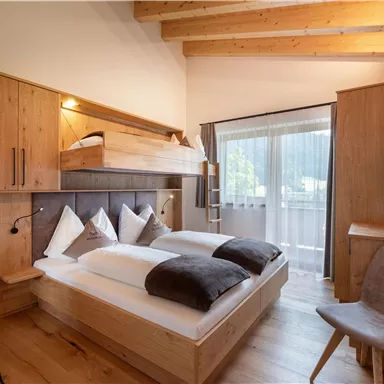 Ein modernes Schlafzimmer mit Holzdekor und großen Fenstern. Es gibt ein Doppelbett und ein gemütliches Zimmer mit einem Stuhl.