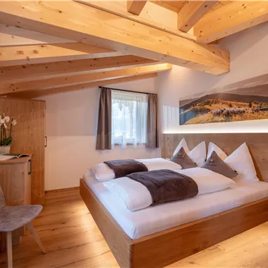 Ein modernes Schlafzimmer mit Holzdecke und warmen Farbtönen. Das Bett ist komfortabel und die Dekoration schafft eine gemütliche Atmosphäre.