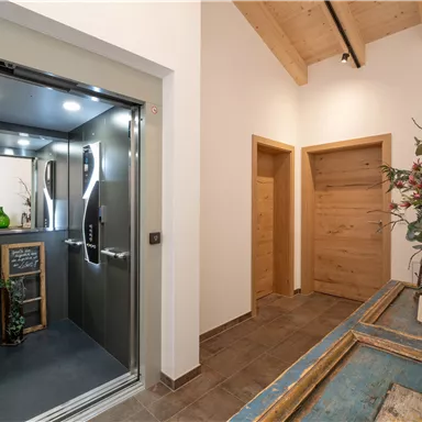 Ein moderner Flur mit einem Aufzug und hellen Holztüren. Die Wände sind in neutralen Farben gehalten und es gibt dekorative Pflanzen.