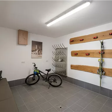 Ein moderner Hauswirtschaftsraum mit einem Fahrrad und Sportschuhen. An der Wand sind Skier und eine praktische Aufbewahrungslösung montiert.