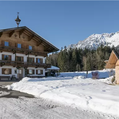 Ein traditionelles Holzhaus im Schnee mit einem malerischen Berg im Hintergrund. Die klare Winterlandschaft vermittelt eine ruhige und einladende Atmosphäre.