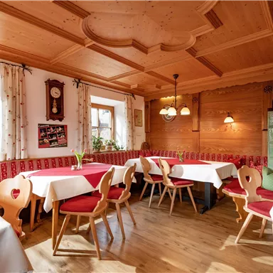 Ein gemütliches Restaurant mit holzvertäfelten Wänden. Tische mit roten Tischdecken und Stühlen sind für Gäste vorbereitet.