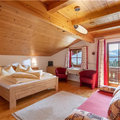 Ein gemütliches Schlafzimmer mit Holzdecke und großen Fenstern. Es gibt ein Doppelbett, zwei rote Sessel und eine schöne Aussicht auf die Berge.