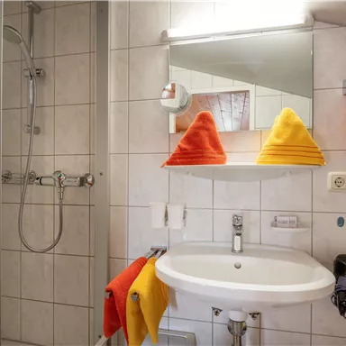 Ein modernes Badezimmer mit einer Dusche und einem Waschbecken. Bunte Handtücher in Gelb und Rot sorgen für einen frischen Akzent.