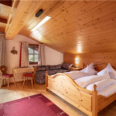 Ein gemütliches Schlafzimmer mit Holzwänden und einem großen Bett. Darin befinden sich auch ein gemütlicher Sitzbereich und große Fenster mit Blick nach draußen.
