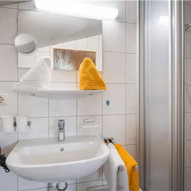 Ein modernes Badezimmer mit einer Duschkabine und einem Waschbecken. Handtücher in orange und weiß sind ordentlich platziert.