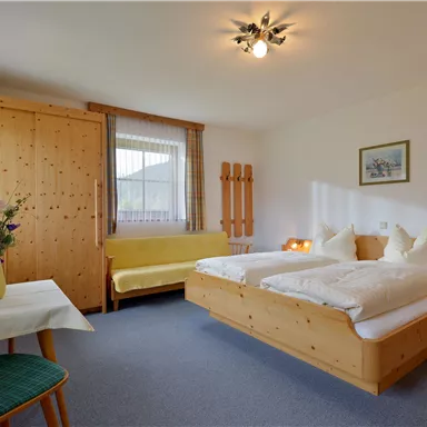 Ein gemütliches Schlafzimmer mit zwei Betten und einem Holzschrank. Es gibt einen kleinen Tisch mit einer Blumenvase und eine Sitzgelegenheit.