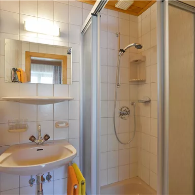 Ein kleines, helles Badezimmer mit Dusche, Waschbecken und Spiegel. Die Wände sind gefliest und es gibt ein Handtuch.