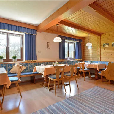 Ein gemütliches Restaurant mit Holzwänden und blauen Vorhängen. Es gibt Tische mit Tischdecken und „Pflanzen“ auf jedem Tisch.