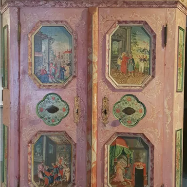 An artistically designed, pink-colored cabinet with colorful paintings on the doors. The images depict various scenes from everyday life and historical representations.