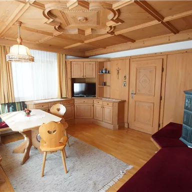 Ein gemütliches Wohnzimmer mit Holzmöbeln und einer warmen Atmosphäre. Der Raum hat einen Essbereich und einen traditionellen Ofen.