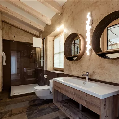 Ein modernes Badezimmer mit Holzverkleidung und zwei runden Spiegeln. Der Raum ist hell und einladend, mit einer Dusche und einem eleganten Waschbecken.
