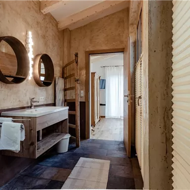 Ein modernes Badezimmer mit Holz- und Steinakzenten. Es verfügt über einen eleganten Waschbereich und große Spiegel.