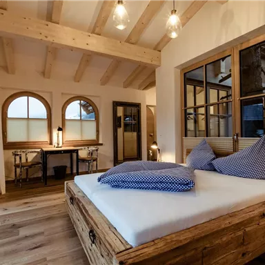 Ein modernes Schlafzimmer mit Holzdetails und großen Fenstern. Das Zimmer ist mit einem gemütlichen Bett und einem kleinen Arbeitsplatz eingerichtet.
