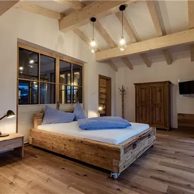 Ein modernes Schlafzimmer mit Holzboden und Holzdecke. Das Zimmer ist gemütlich eingerichtet mit einem großen Bett und einer Fensterfront.