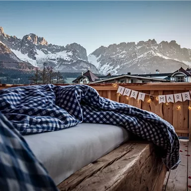 Eine gemütliche Terrasse mit Blick auf beeindruckende Berggipfel. Hinter einem Bett mit einer karierten Decke hängt ein "Just Married"-Schild.