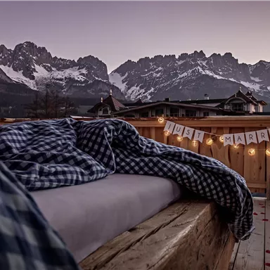 Eine romantische Terrasse mit einer Decke und Blick auf die Berge. Im Hintergrund hängt ein "Just Married"-Schild.