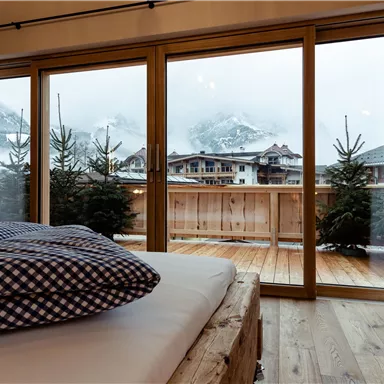 Ein gemütliches Schlafzimmer mit einem Bett und einer schönen Aussicht auf die Berge. Draußen sieht man Bäume und einen Holzbalcony.