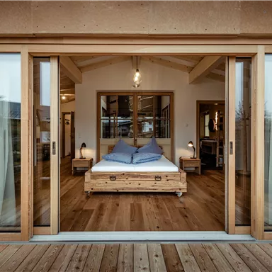 Ein modernes Schlafzimmer mit Holzmöbeln und großen Fenstern. Der Raum ist hell und einladend, mit Blick auf die Veranda.