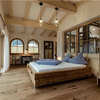 Ein modernes Schlafzimmer mit Holzfußboden und großen Fenstern. Das Schlafzimmer ist gemütlich eingerichtet mit einem Bett und einem kleinen Tisch.
