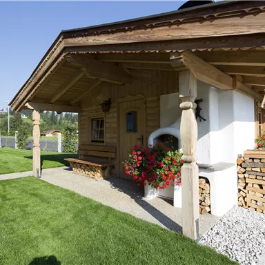 Ein charmantes Holzhaus mit einem gepflegten Garten und Blumen. Der klare Himmel und die umliegende Natur schaffen eine einladende Atmosphäre.