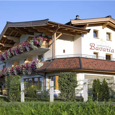 Ein charmantes Gebäude mit dem Namen "Bavaria" in einer malerischen Landschaft. Bunte Blumenkästen und eine grüne Wiese umgeben das Haus.