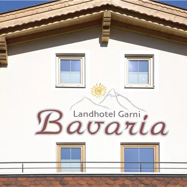 Ein Landhotel mit dem Namen "Bavaria" an der Fassade. Es hat eine helle Wand und drei Fenster sowie ein traditionelles Dach.
