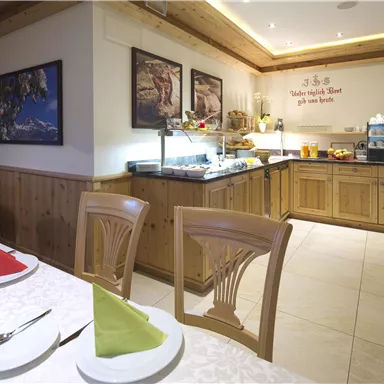 Ein einladendes Restaurant mit Holzdekor und hellen Wänden. Am Buffet stehen verschiedene Speisen bereit, während Tischdekoration in Rot und Grün coloriert ist.