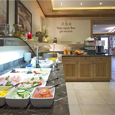 Ein reichhaltiges Frühstücksbuffet mit verschiedenen frischen Lebensmitteln, darunter Obst, Gemüse und Aufschnitt. Der Raum ist hell und einladend mit Holzdecken und gemütlicher Atmosphäre.