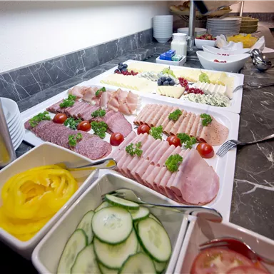 Ein reichhaltiges Frühstücksbuffet mit verschiedenen Wurst- und Käsesorten. Daneben frisches Gemüse und Saucen auf einem Stehtisch.