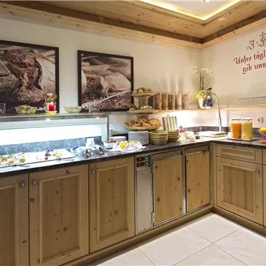 Ein einladendes Frühstücksbuffet mit verschiedenen Speisen, Obst und Getränken. Die Holzverkleidung und die dekorativen Bilder schaffen eine gemütliche Atmosphäre.