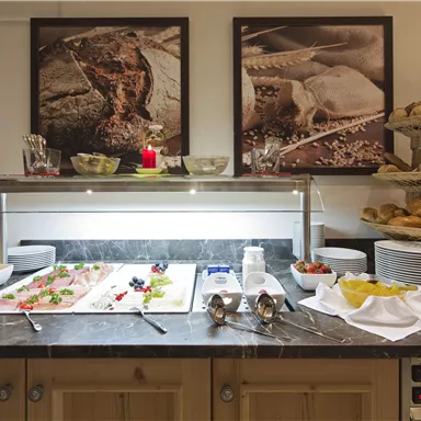 Ein Buffet mit einer Auswahl an frischen Snacks und Brötchen. Im Hintergrund hängen an der Wand Bilder von Lebensmitteln.