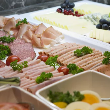 Ein reichhaltiges Buffet mit verschiedenen Aufschnittsorten, Käsestücken und frischen Trauben. Die Speisen sind ästhetisch angeordnet und mit frischer Petersilie dekoriert.
