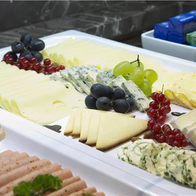 Ein reichhaltiges Käse- und Wurstbrett mit Trauben und roten Johannisbeeren. Vielfalt an Käse und Wurstarrangements auf einem eleganten weißen Teller.