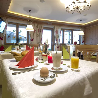 Ein gemütliches Frühstück in einem hellen Restaurant. Der Tisch ist eingedeckt mit Tellern, Getränken und frischen Brötchen.