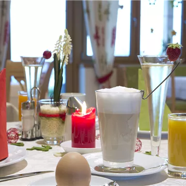 Ein schön gedeckter Tisch mit Frühstück. Es gibt ein gekochtes Ei, verschiedene Getränke und dekorative Elemente auf dem Tisch.