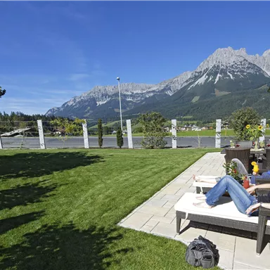Eine entspannte Terrasse mit Liegen und Blick auf die Berge. Der Himmel ist klar und die Landschaft ist grün und einladend.